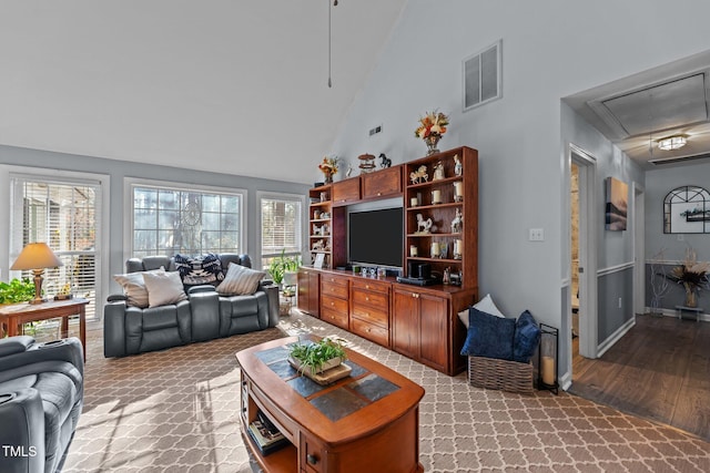 living area with high vaulted ceiling, visible vents, baseboards, light wood finished floors, and attic access