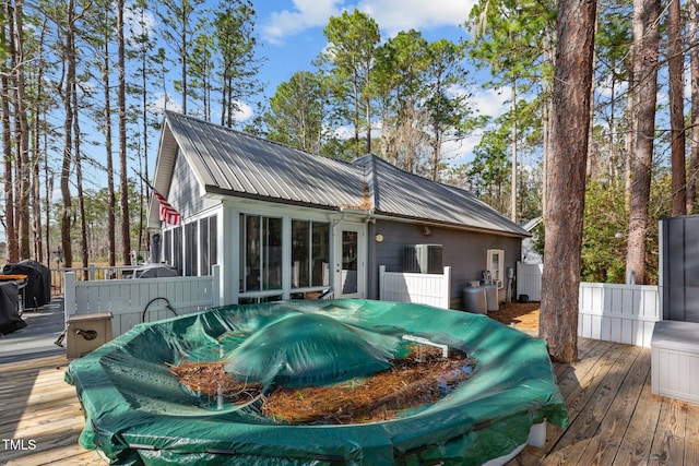 back of property featuring metal roof, a wooden deck, and a sunroom