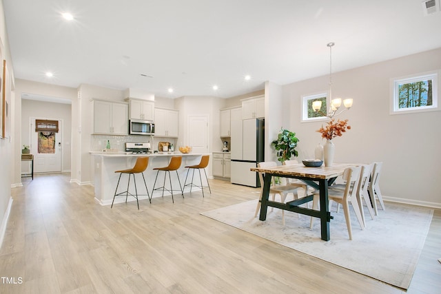 dining space with an inviting chandelier, visible vents, light wood-type flooring, and baseboards