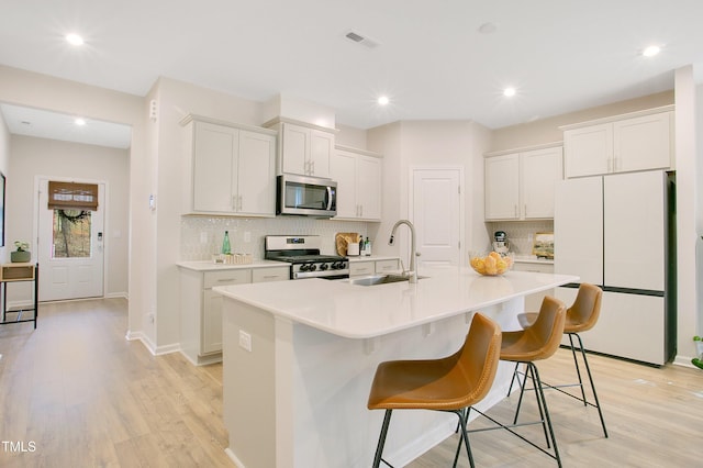 kitchen featuring visible vents, an island with sink, light countertops, stainless steel appliances, and a sink