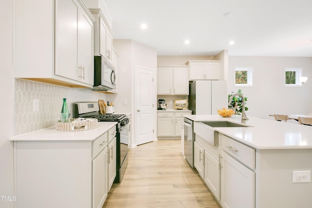 kitchen featuring a center island with sink, light wood-style flooring, a sink, stainless steel appliances, and light countertops