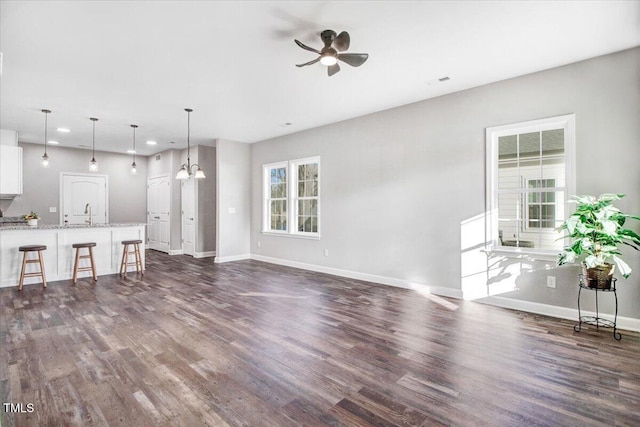 unfurnished living room with dark wood-style floors, baseboards, and ceiling fan with notable chandelier