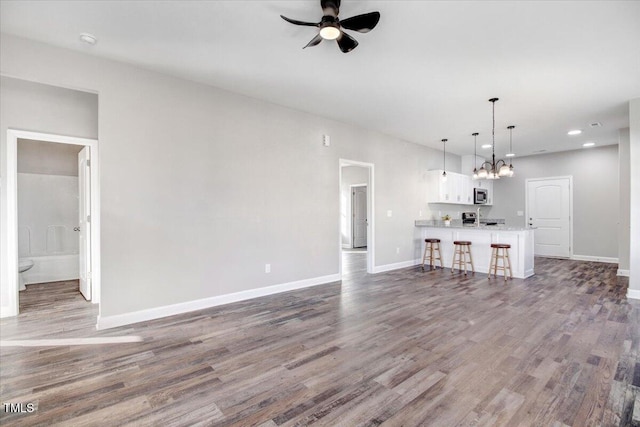 unfurnished living room with baseboards, wood finished floors, and ceiling fan with notable chandelier