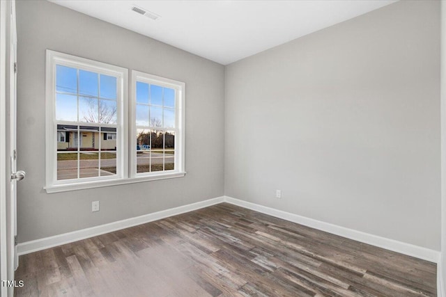 empty room with baseboards, visible vents, and dark wood finished floors