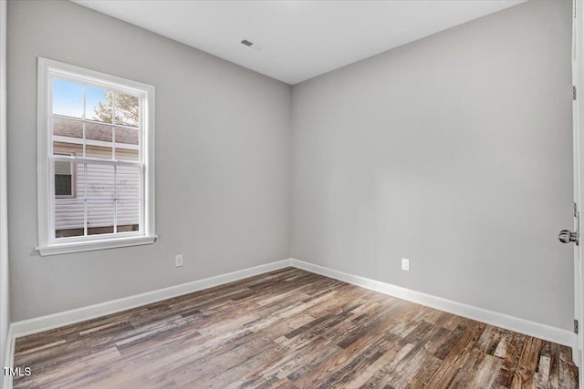 spare room with wood finished floors, visible vents, and baseboards