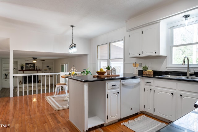 kitchen featuring a peninsula, a sink, white cabinets, dishwasher, and dark countertops