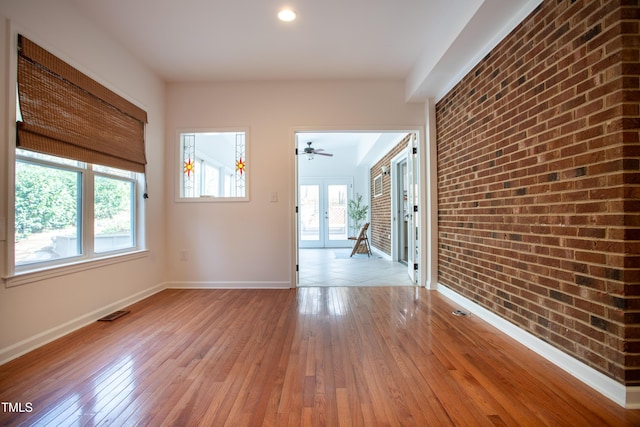 empty room featuring hardwood / wood-style floors, visible vents, baseboards, and brick wall