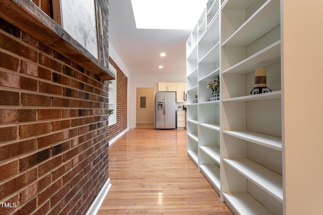 hall with light wood-style flooring, recessed lighting, and brick wall