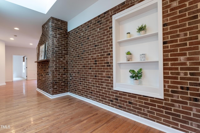 interior space featuring built in shelves, brick wall, baseboards, recessed lighting, and wood finished floors