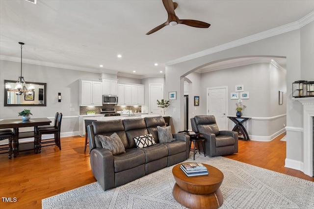 living room featuring baseboards, arched walkways, light wood-style flooring, and ceiling fan with notable chandelier