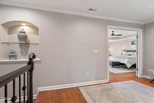 corridor featuring baseboards, wood finished floors, visible vents, and ornamental molding