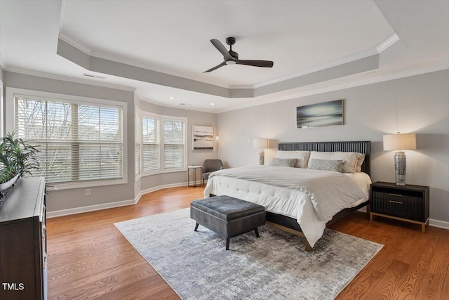 bedroom featuring light wood finished floors, baseboards, crown molding, and a tray ceiling