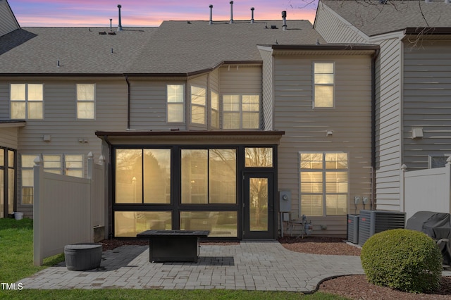 rear view of house featuring fence, roof with shingles, cooling unit, a sunroom, and a patio