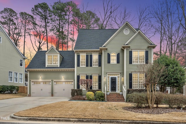 colonial home featuring concrete driveway, a garage, and a shingled roof