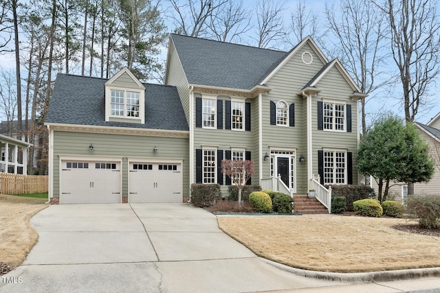 colonial-style house with roof with shingles, concrete driveway, an attached garage, and fence