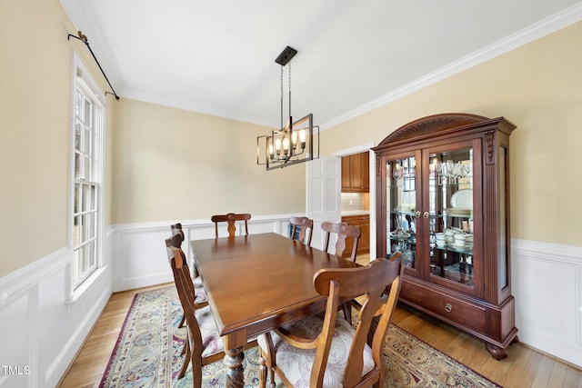 dining room with a wainscoted wall, a chandelier, ornamental molding, and light wood finished floors