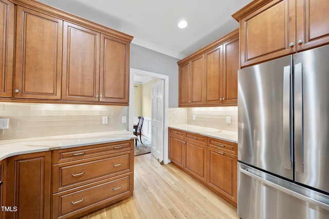 kitchen featuring brown cabinets, light wood-style flooring, light stone countertops, and freestanding refrigerator