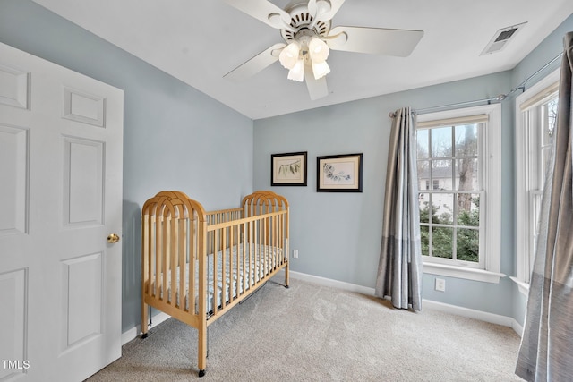 carpeted bedroom featuring visible vents, baseboards, a nursery area, and ceiling fan