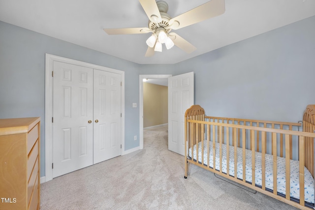 bedroom featuring a crib, a ceiling fan, a closet, carpet, and baseboards