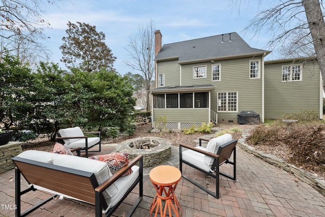 rear view of property with a patio, a sunroom, an outdoor living space with a fire pit, a shingled roof, and a chimney