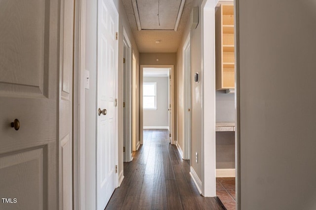 hall featuring dark wood-style flooring, attic access, and baseboards