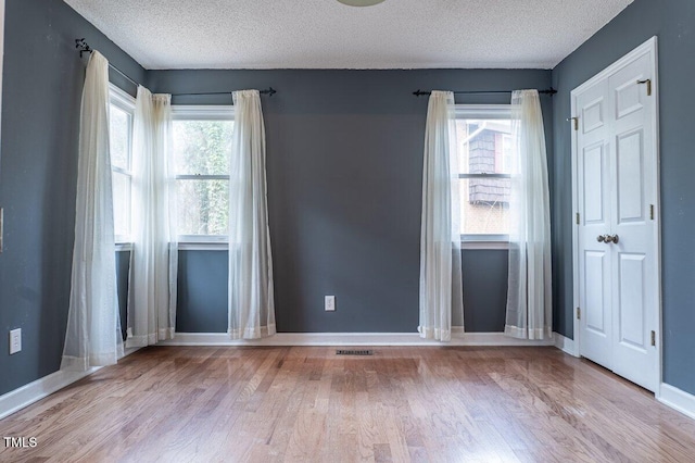 unfurnished room with visible vents, a textured ceiling, baseboards, and wood finished floors