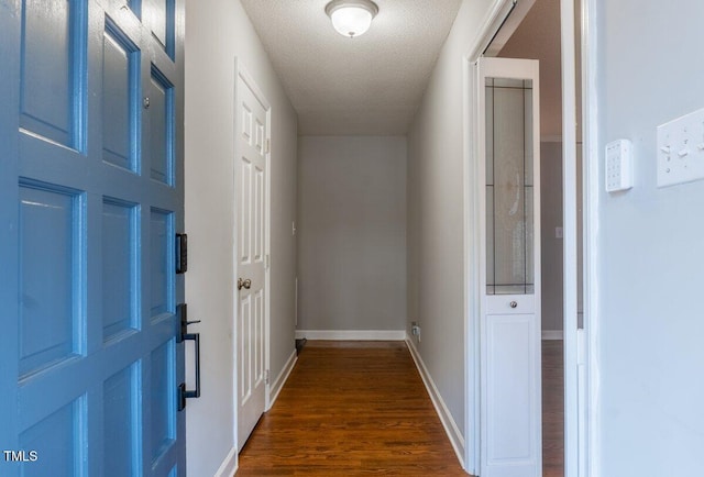 corridor with a textured ceiling, dark wood finished floors, and baseboards