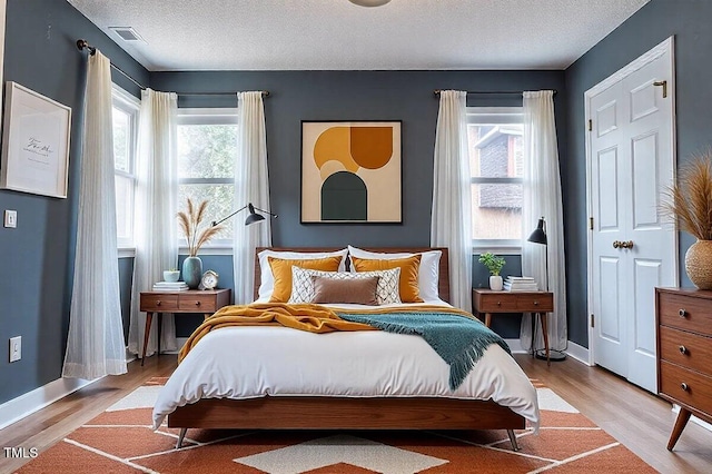 bedroom with a textured ceiling, light wood-style flooring, multiple windows, and visible vents