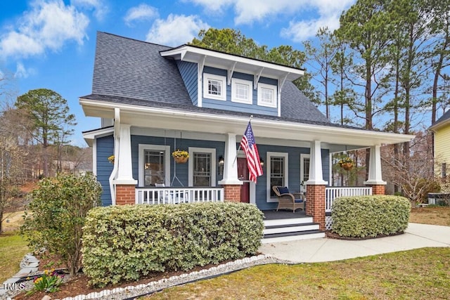 view of front facade with brick siding, a porch, and a shingled roof