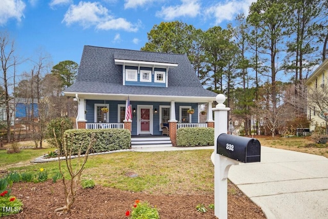 view of front facade featuring a porch, a front yard, and roof with shingles