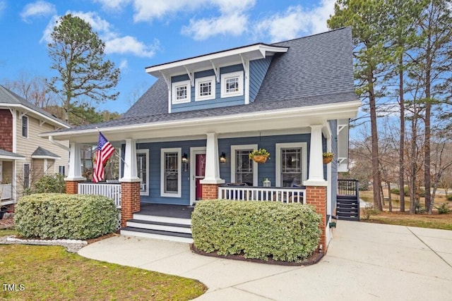 view of front of house featuring roof with shingles, covered porch, and brick siding