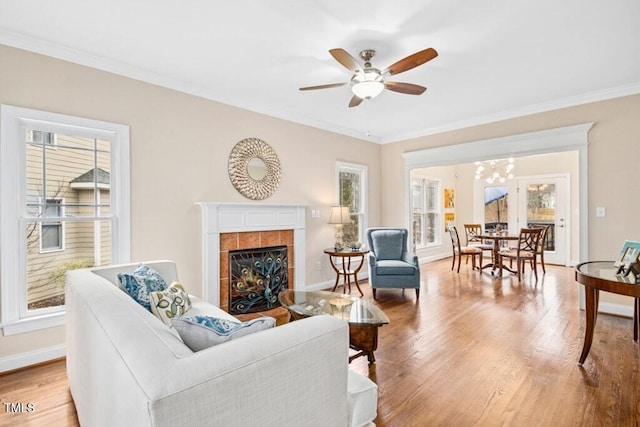 living room featuring crown molding, a fireplace, baseboards, and light wood finished floors