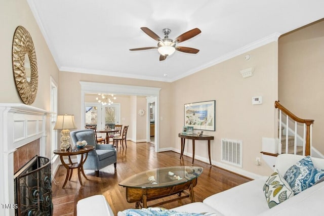 living area featuring visible vents, crown molding, a tiled fireplace, stairs, and wood finished floors