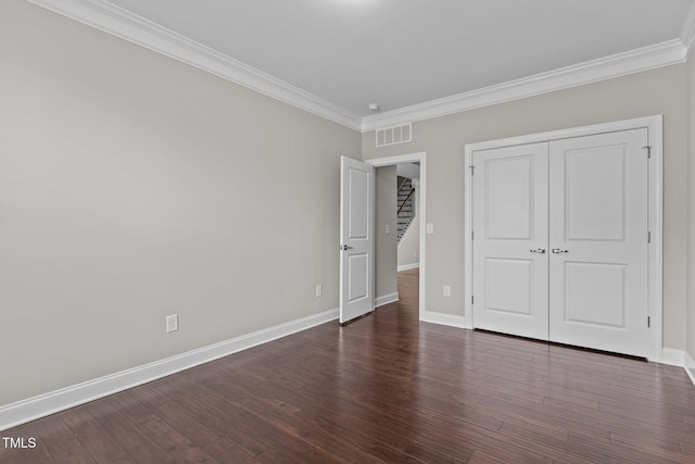 unfurnished bedroom featuring visible vents, baseboards, dark wood finished floors, a closet, and crown molding