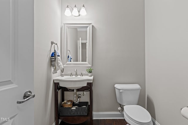 half bath featuring toilet, wood finished floors, baseboards, and a sink