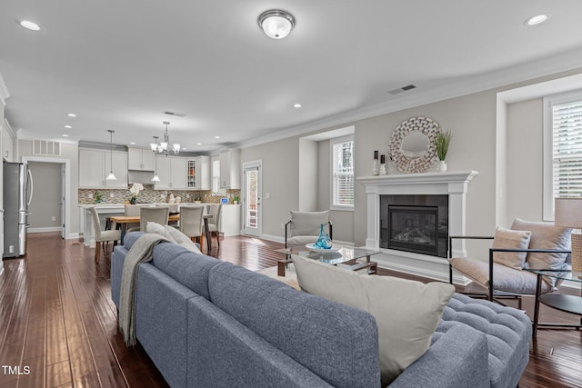 living room featuring dark wood-style floors, visible vents, a fireplace, crown molding, and a chandelier