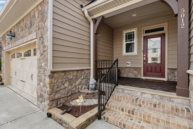 doorway to property featuring a garage, stone siding, and concrete driveway