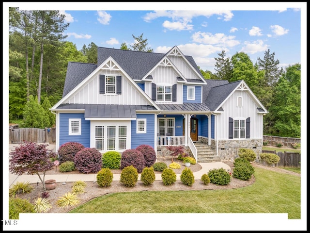 view of front of house with a front yard, fence, roof with shingles, a standing seam roof, and a porch