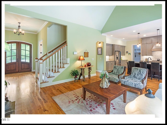 living area with stairway, baseboards, light wood finished floors, french doors, and crown molding