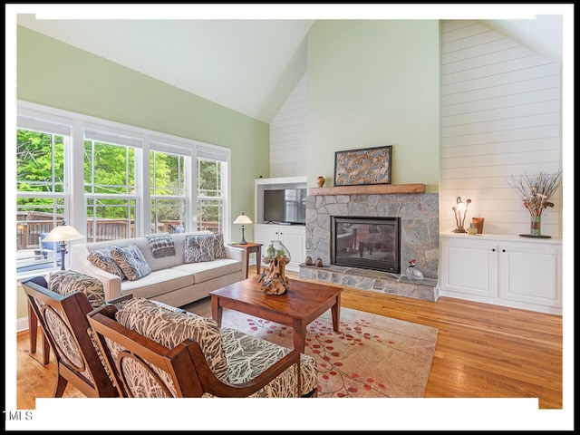 living room with high vaulted ceiling, light wood-style flooring, and a fireplace