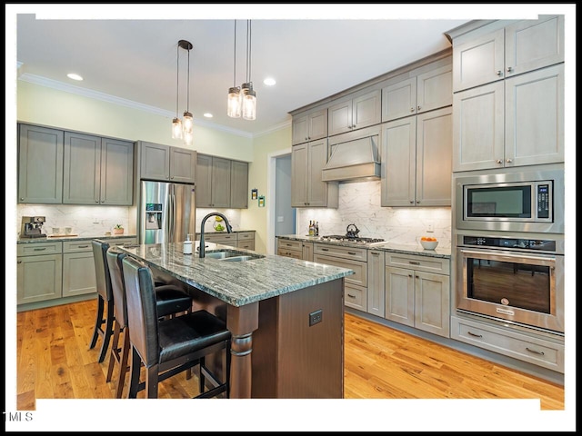 kitchen with light wood finished floors, a sink, stainless steel appliances, custom range hood, and crown molding