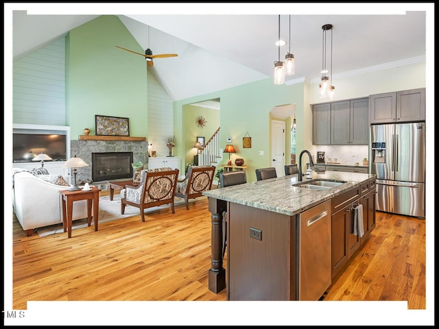 kitchen with light wood-style flooring, a sink, light stone counters, stainless steel appliances, and a stone fireplace