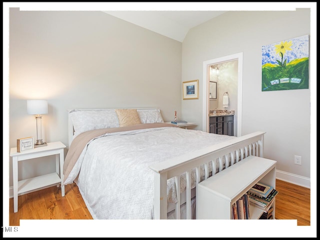 bedroom featuring ensuite bathroom, baseboards, light wood-type flooring, and lofted ceiling