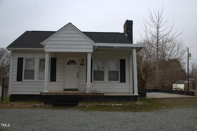 bungalow-style home with crawl space, covered porch, a chimney, and roof with shingles