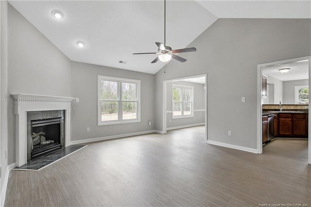 unfurnished living room featuring baseboards, a ceiling fan, wood finished floors, vaulted ceiling, and a high end fireplace