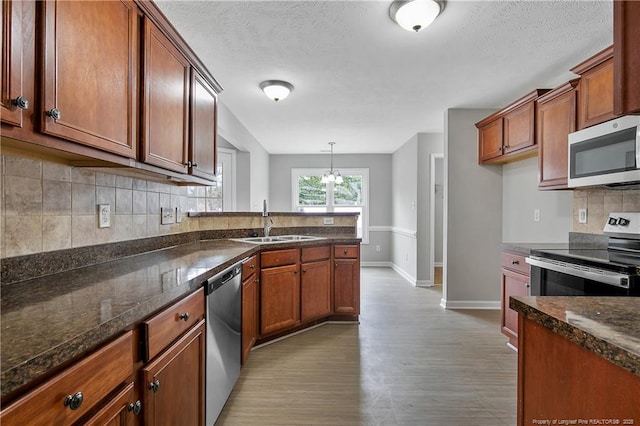 kitchen with brown cabinetry, wood finished floors, a sink, stainless steel appliances, and backsplash