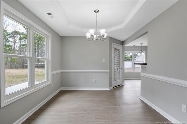unfurnished dining area with a chandelier, a tray ceiling, wood finished floors, and visible vents