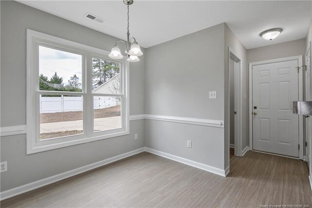 unfurnished dining area featuring visible vents, a notable chandelier, baseboards, and wood finished floors