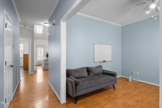 sitting room with crown molding, a skylight, baseboards, and light wood-type flooring