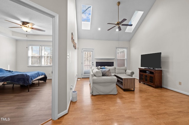 living area with a skylight, a ceiling fan, light wood-type flooring, and baseboards